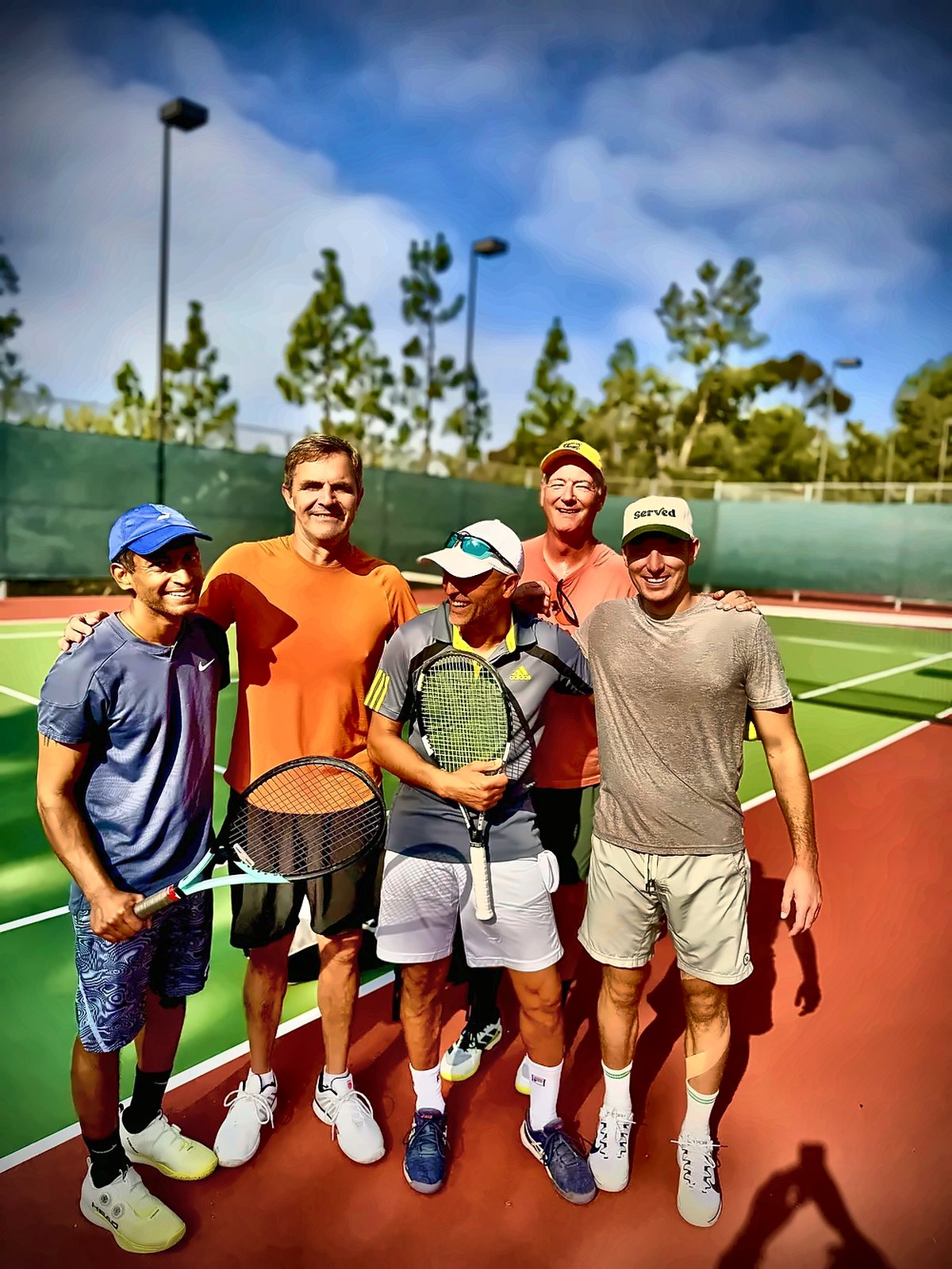 Adult tennis clinic players smiling with Coach Fawz after a session