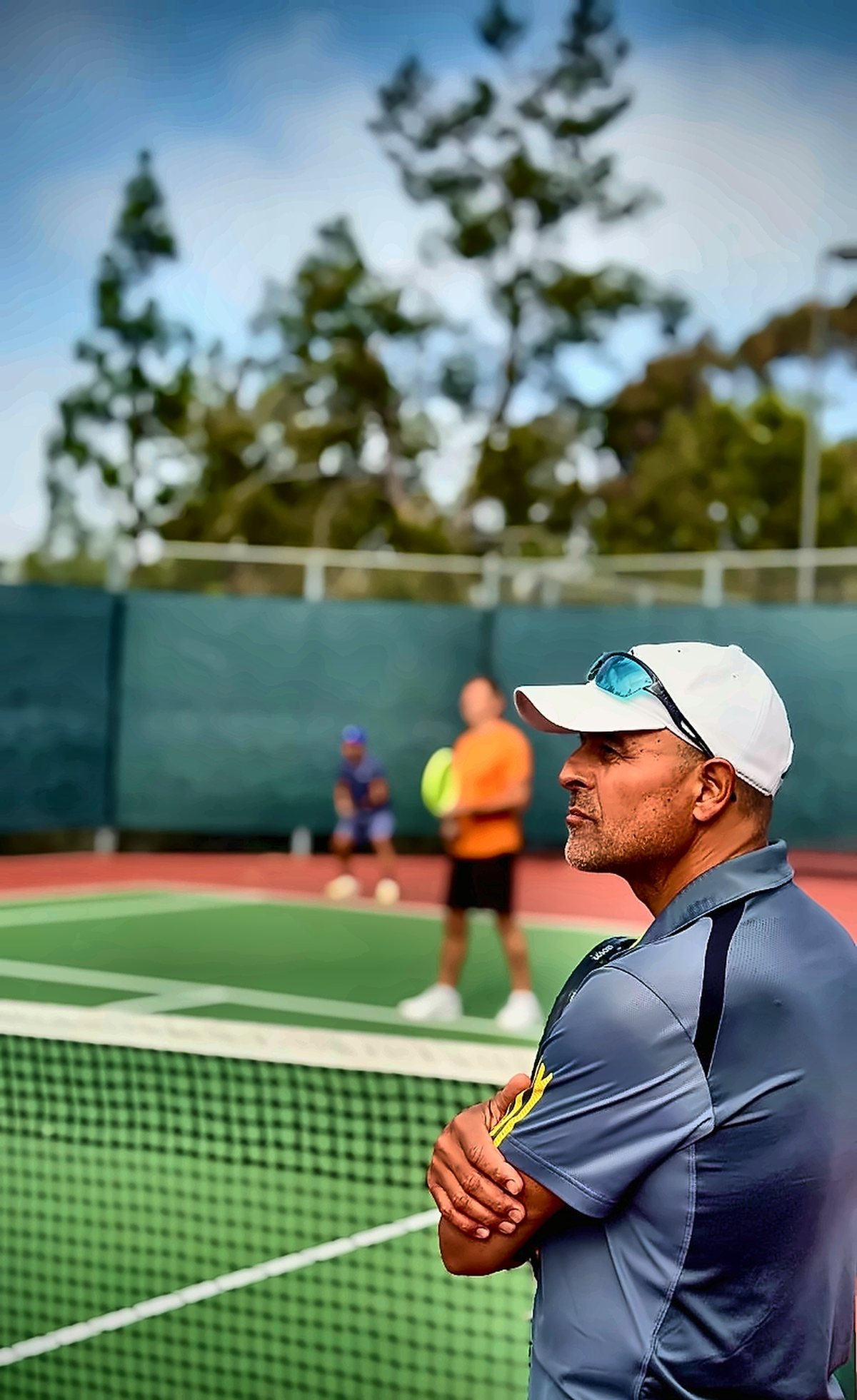 Coach Fawz standing courtside with arms crossed during a lesson