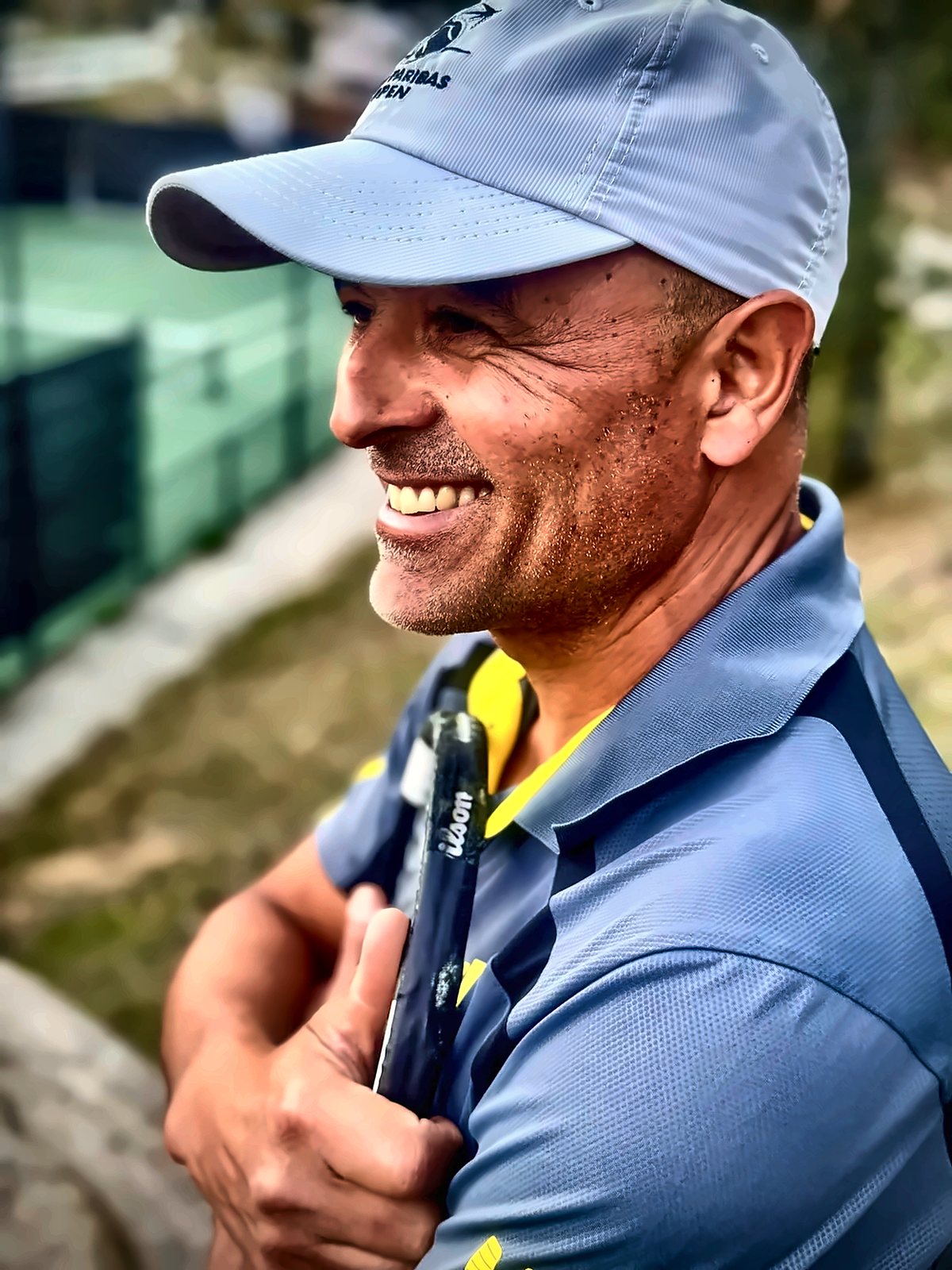 Coach Fawz Ksikes smiling courtside with his racket