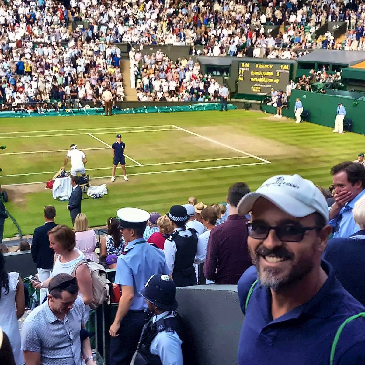 Fawz courtside at a grass-court tournament with Roger Federer playing behind him