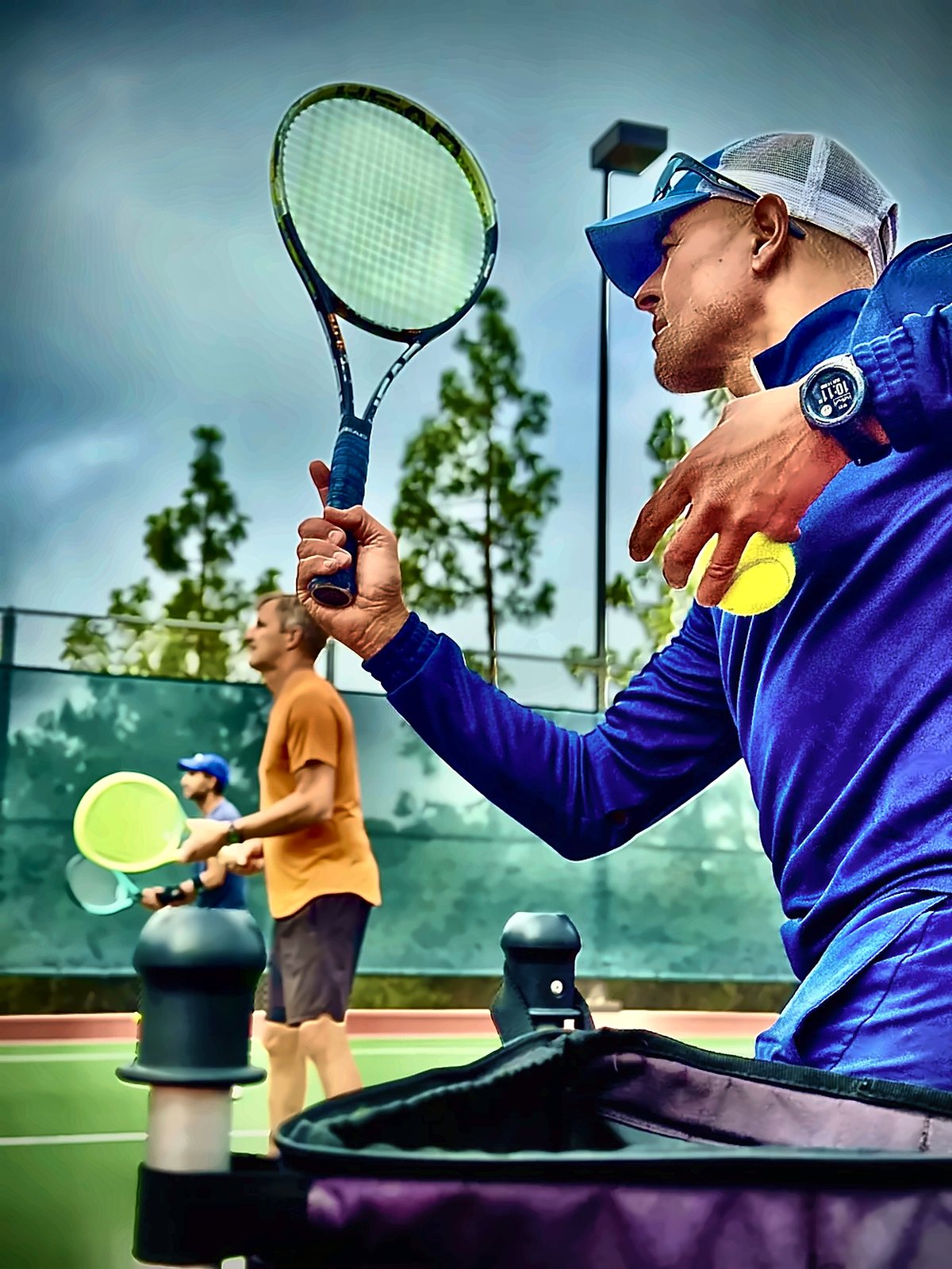 Coach Fawz with racket raised, feeding balls to an adult student